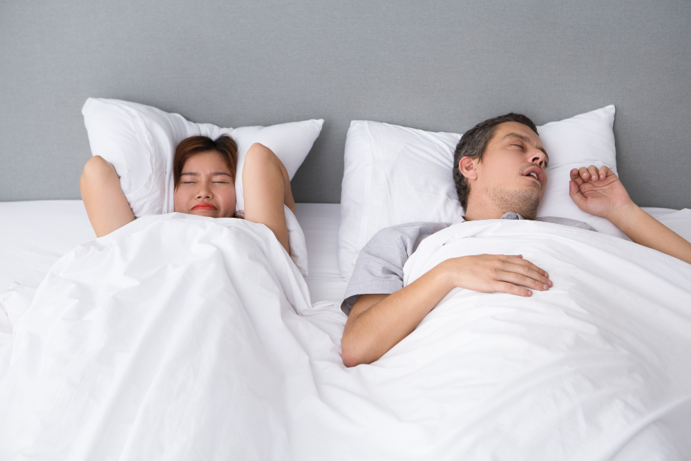 Woman lying next to snoring husband angrily covering her ears