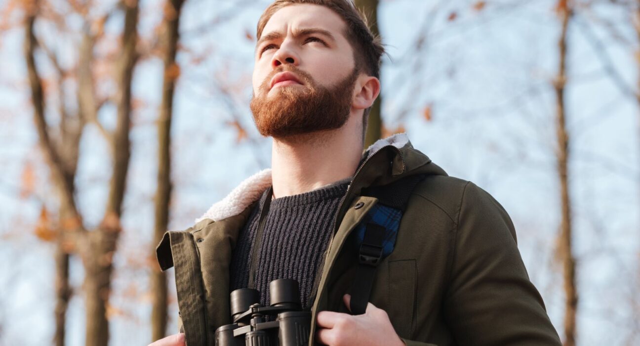 Bearded man wearing a backpack gazing out while in the woods