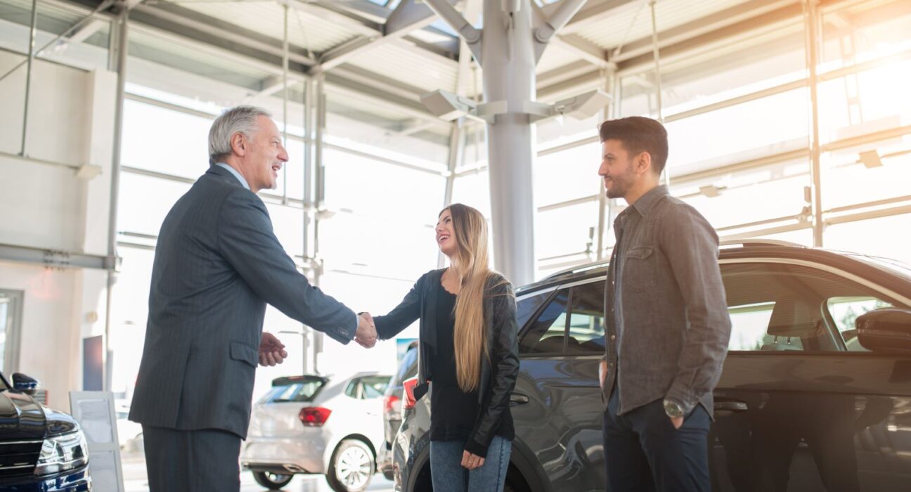 A car salesman shaking hands with clients after making a car deal