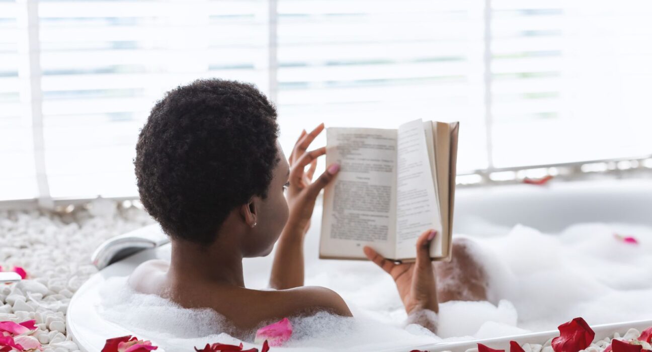 Young black female reading a book while having a tub bath