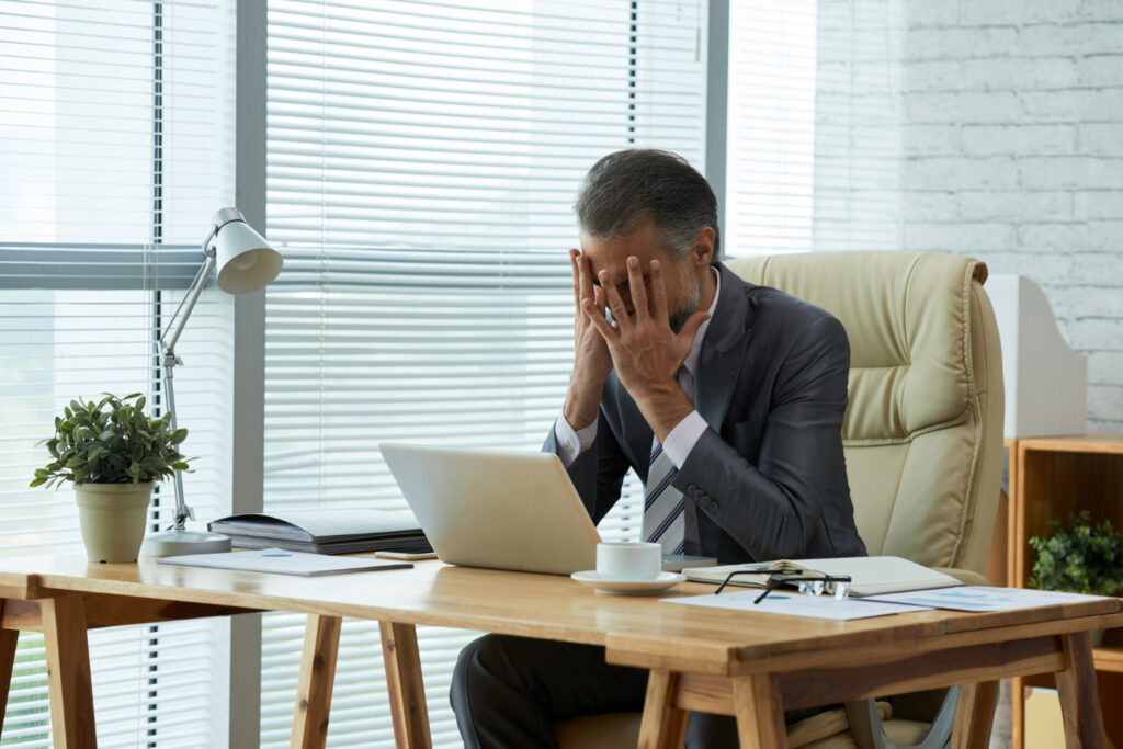Businessman seated at desk with his hands on his face frustrated by failure