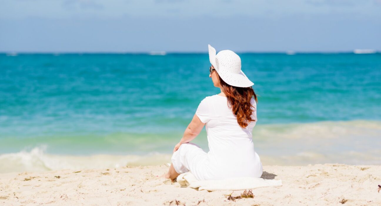 A woman sitting upright on the beach enjoying the ocean view