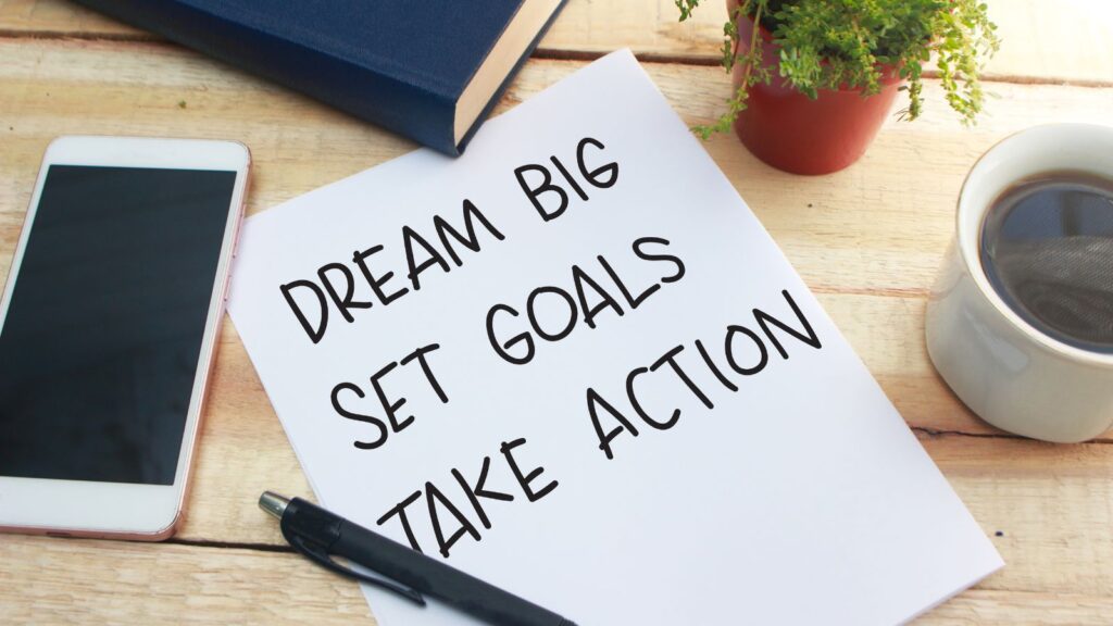 "Dream big, set goals, take action" written on a white sheet of paper