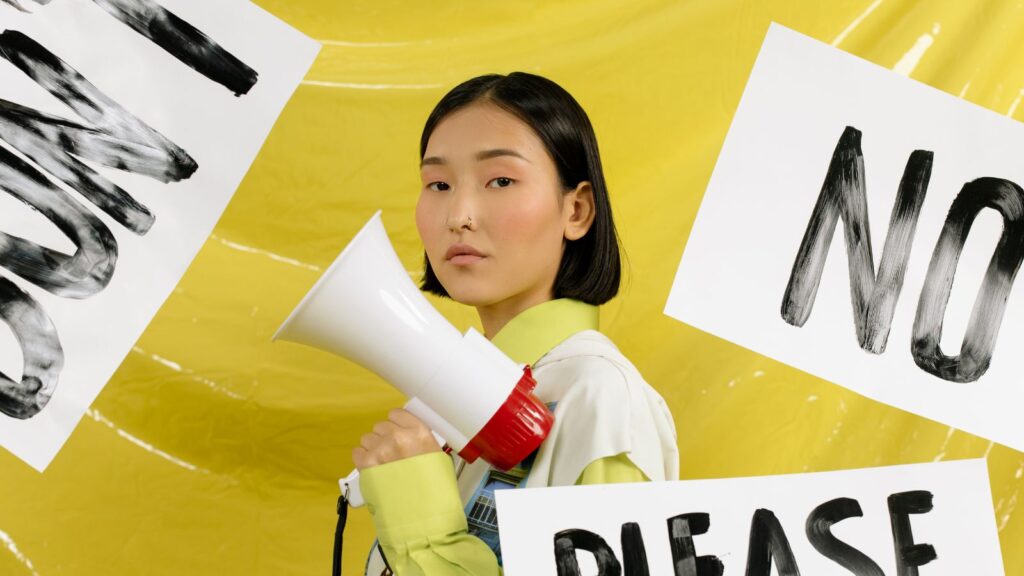 Woman holding a megaphone with paper signs saying "no" and "please"